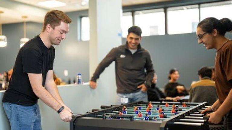 Photos shows students playing foosball in the student lounge. 